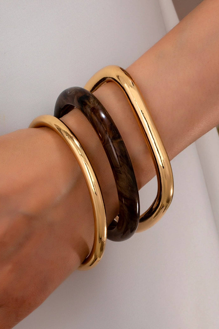 Gold and brown bangles on a wrist against a neutral background